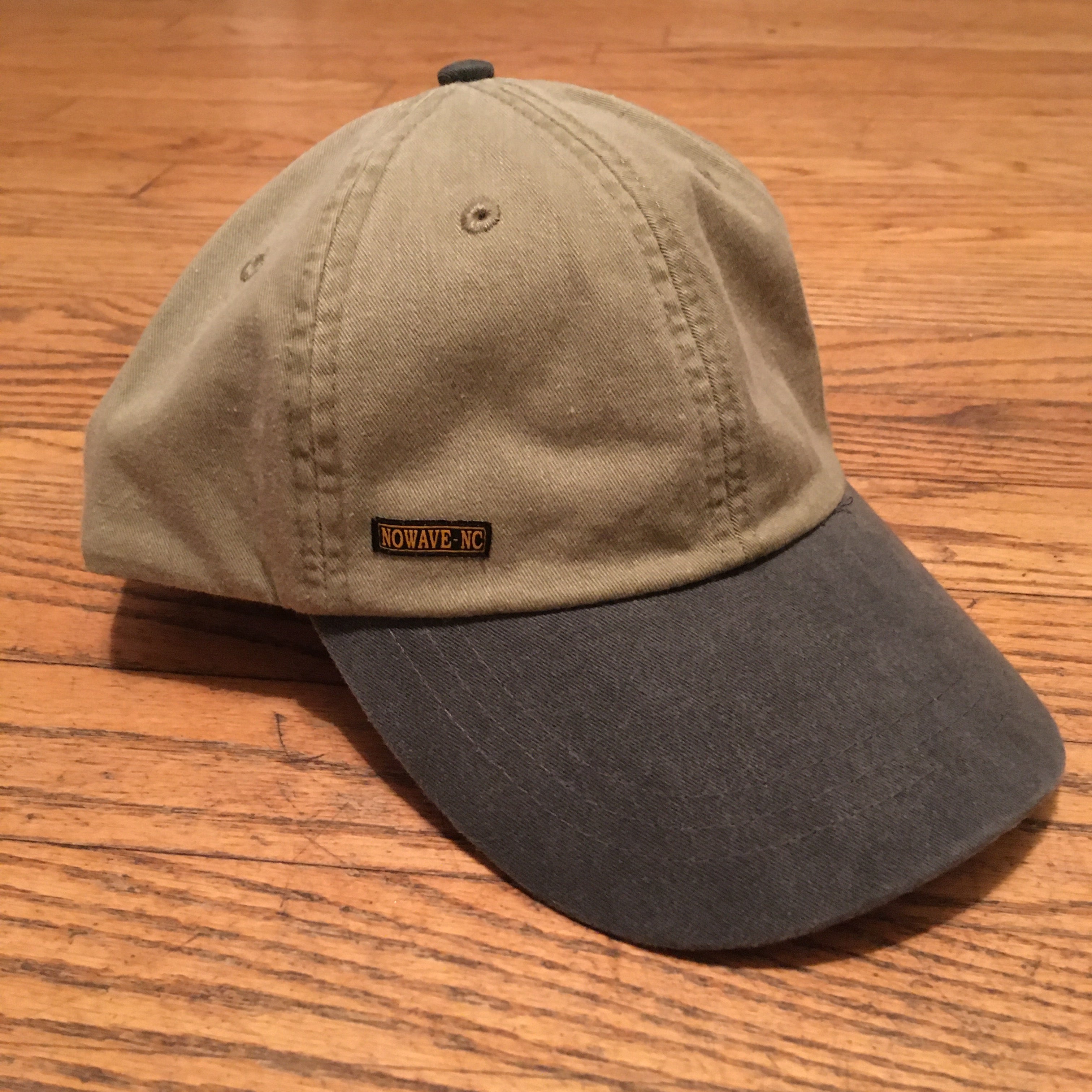 The 'MILLIGAN' Two Tone Dad Hat.  A classic.  All time.  Never goes bad.  No expiration date.  Always gold my friends!  Delivered in a khaki cap with either a washed blue or washed black bill and button at far top.  Features a genuine leather strap with gold-colorored clasp at rear.  Super breathable liner on the inside sets this hat a couple notches above the rest.  This thing is yer' go-to.  Just ask a dude in a tractor with a/c...and possibly a radio too.