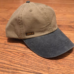 Load image into Gallery viewer, The &#39;MILLIGAN&#39; Two Tone Dad Hat.  A classic.  All time.  Never goes bad.  No expiration date.  Always gold my friends!  Delivered in a khaki cap with either a washed blue or washed black bill and button at far top.  Features a genuine leather strap with gold-colorored clasp at rear.  Super breathable liner on the inside sets this hat a couple notches above the rest.  This thing is yer&#39; go-to.  Just ask a dude in a tractor with a/c...and possibly a radio too.
