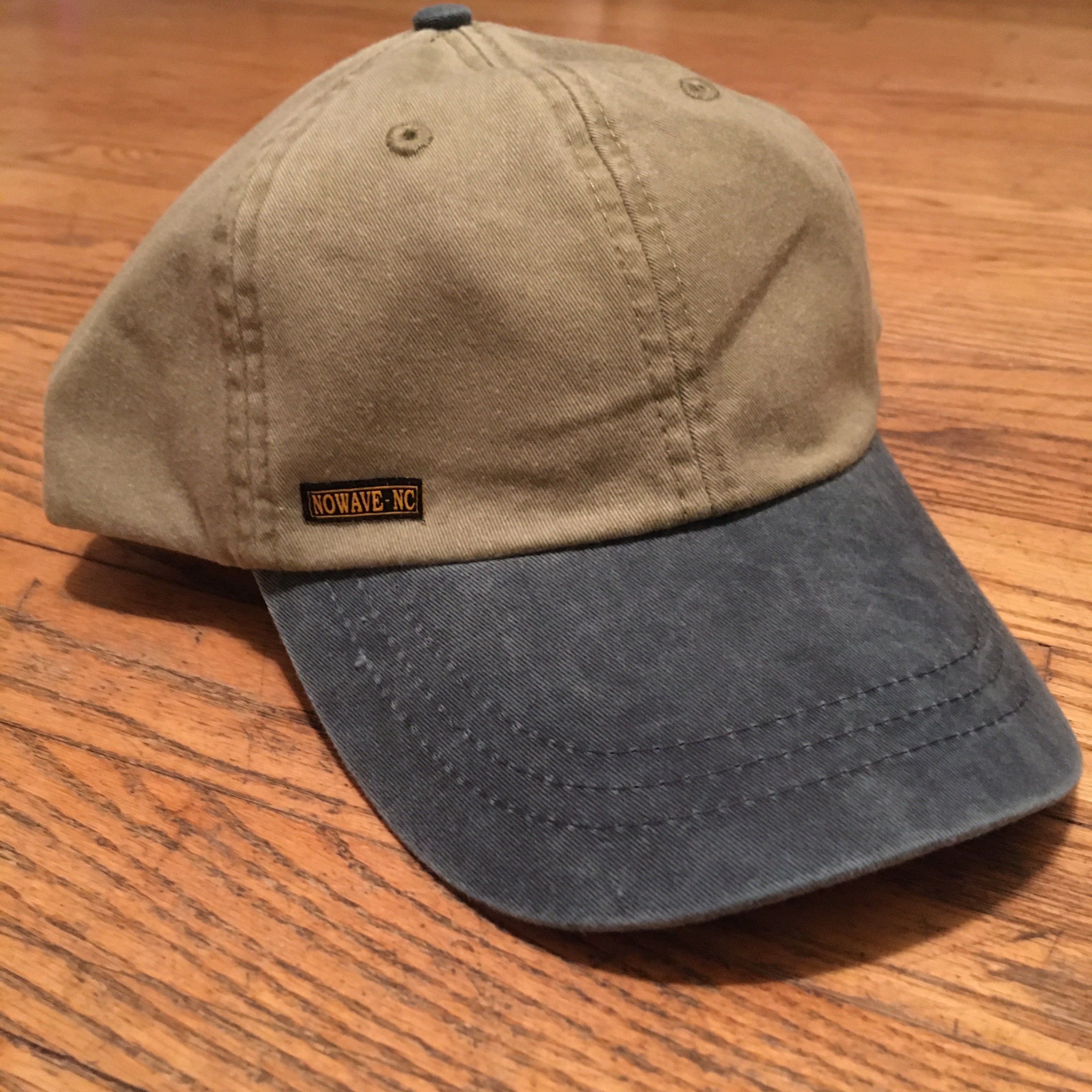 The 'MILLIGAN' Two Tone Dad Hat.  A classic.  All time.  Never goes bad.  No expiration date.  Always gold my friends!  Delivered in a khaki cap with either a washed blue or washed black bill and button at far top.  Features a genuine leather strap with gold-colorored clasp at rear.  Super breathable liner on the inside sets this hat a couple notches above the rest.  This thing is yer' go-to.  Just ask a dude in a tractor with a/c...and possibly a radio too.